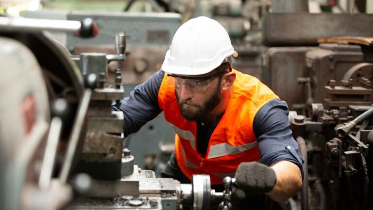 Factory technician in safety gear operating manufacturing automation equipment on a production line