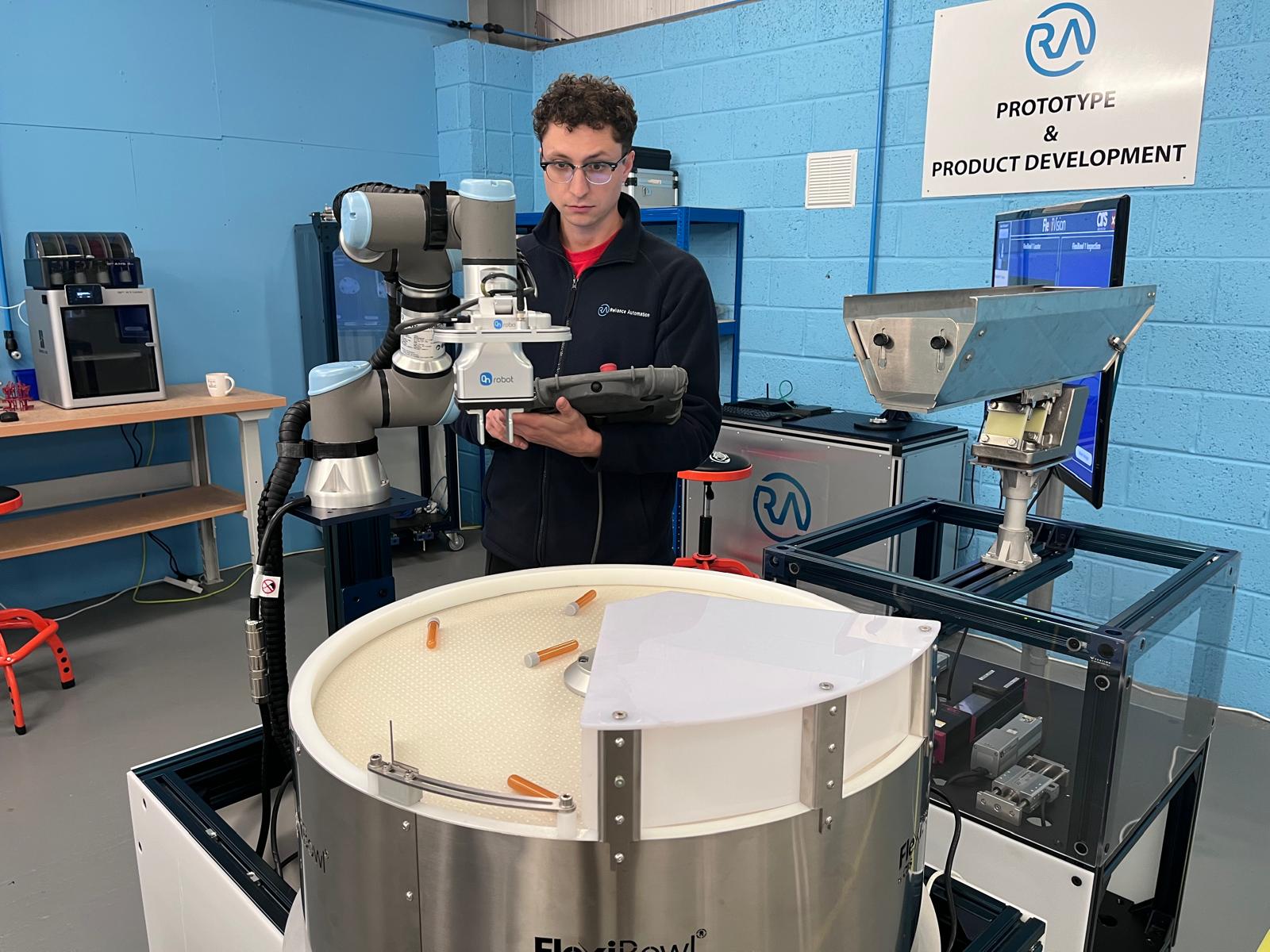 Reliance Automation engineer testing a FlexiBowl part-feeding cell with a collaborative robot in the development lab