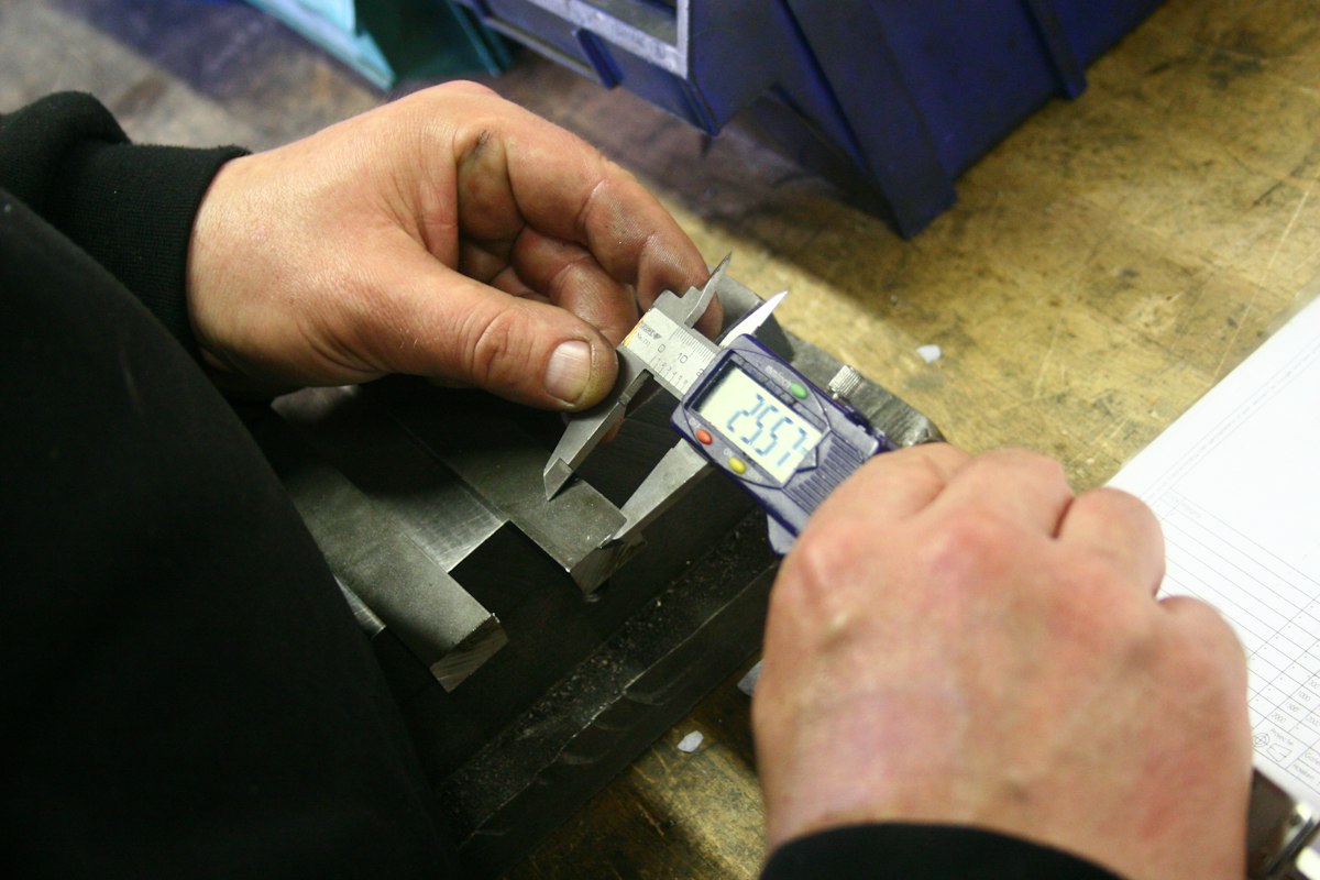 Hands measuring a machined metal part with a digital caliper for quality control