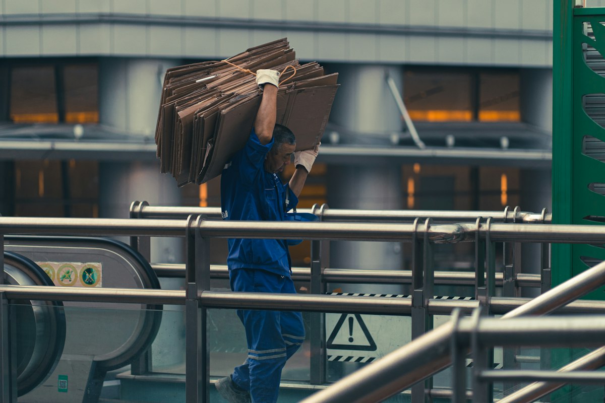 Worker manually carrying heavy cardboard boxes in a factory